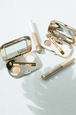 mavi pastel arka plan üzerinde kaş ürünleri. Kaşlar için balmumu, göz farı ve maskara. Kozmetik ürünlerde palmiye yaprağı gölgesi