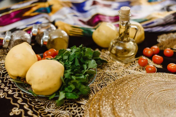 Плоды айвы на столе украшены восточными тканями с орнаментами и золотыми акцентами. Концепция восточной кухни. На столе фрукты, помидоры и травы айвы . — стоковое фото