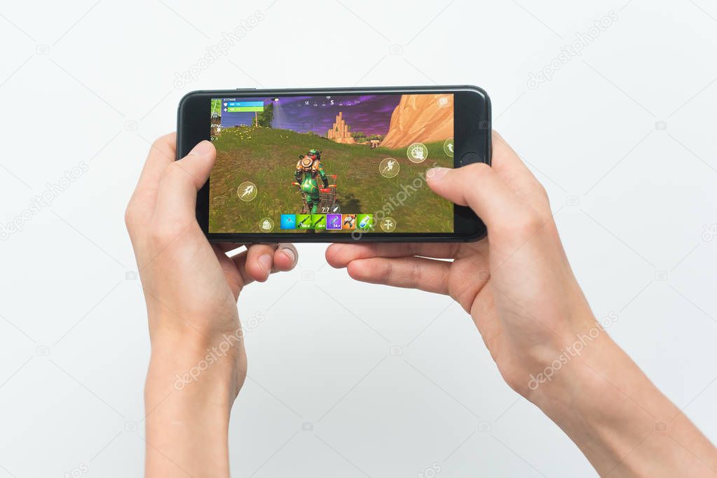 Samara, Russia -07, 29, 2019: A young guy playing Fortnite game on Iphone 8 Plus. Teenage boy holding a phone in his hands with a game Fortnite battle royale on a white background.