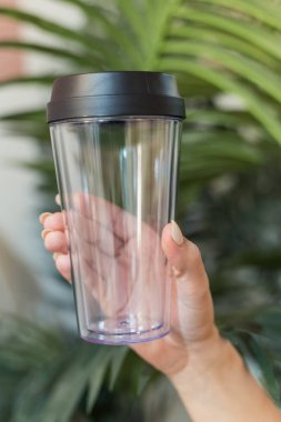 Kız elinde yeşil palmiye yaprakları bir arka plan üzerinde kahve için yeniden kullanılabilir bir bardak tutar. Doğa, ekoloji, plastik geri dönüşüm konsepti bakımı