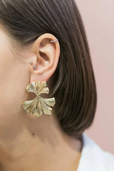 Brincos de ouro redondos elegantes na moda na orelha da menina com corte de cabelo bob. Fundo rosa pastel — Fotografia de Stock