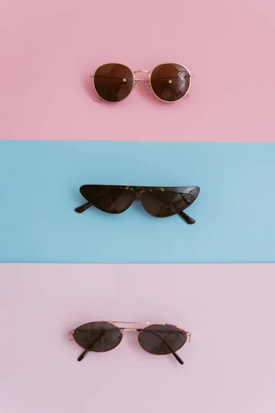 Occhiali da sole immagine elegante su uno sfondo pastello. Tre paia di occhiali con lenti su sfondo rosa e blu. ottica elegante e di tendenza — Foto Stock