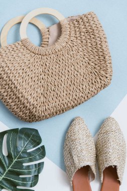 Bej hasır çanta ve katırlar bir pastel arka plan üzerinde. Hasır sepet ve ayakkabı üst görünümü. Palmiye yaprağı ve trendy ve şık aksesuarlar.