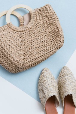 Bej hasır çanta ve katırlar bir pastel arka plan üzerinde. Hasır sepet ve ayakkabı üst görünümü. modaya uygun ve şık aksesuarlar. Trend 2019.
