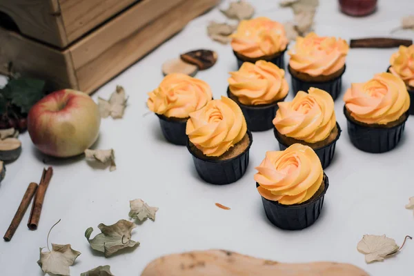 Pastelitos de otoño amarillo y naranja sobre un fondo claro con hojas muertas de otoño, calabazas y manzanas. Dulces de otoño con crema para niños. Magdalenas de zanahoria en el fondo de otoño . — Foto de Stock