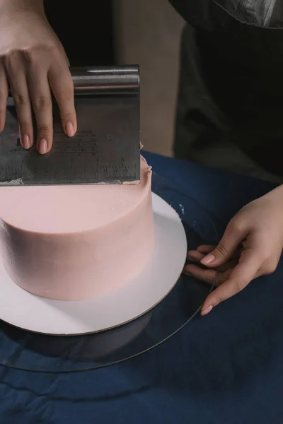 Кондитер выравнивает крем с лопаткой. Мастер тортов выстраивает крем на бежевый свадебный торт . — стоковое фото