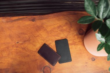 ahşap bir arka plan üzerinde deri lüks telefon kılıfları. bir tencerede bir çiçek arka planda iki eko-deri telefon kapakları. Erkek ve kadın deri aksesuarları