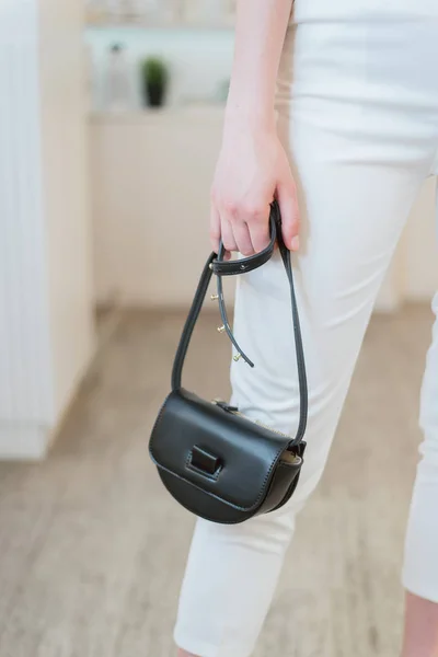 Una piccola borsetta nera in mano a una ragazza vestita di bianco . — Foto Stock