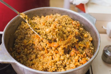 Kazanda mutfakta oryantal pilav pişirmek. Bir kadın kuzu, sığır eti, pirinç, nohut, havuç bir tabak hazırlar