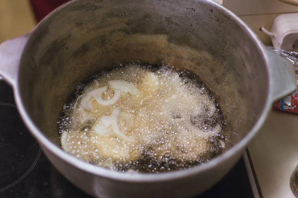 O cozinheiro frita anéis de cebola em uma panela em uma grande quantidade de óleo vegetal . — Fotografia de Stock