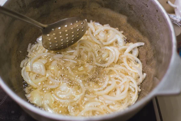 O cozinheiro frita anéis de cebola em uma panela em uma grande quantidade de óleo vegetal . — Fotografia de Stock