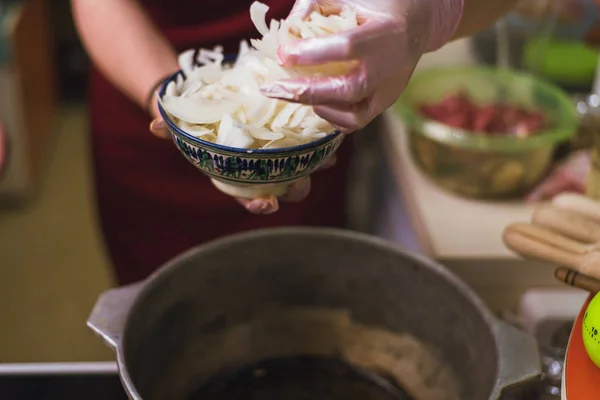 Mulher coloca cebolas em uma panela com manteiga. O cozinheiro frita anéis de cebola em uma panela em uma grande quantidade de óleo vegetal . — Fotografia de Stock