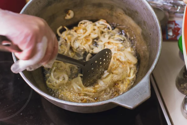 El cocinero fríe aros de cebolla en una sartén en una gran cantidad de aceite vegetal . — Foto de Stock