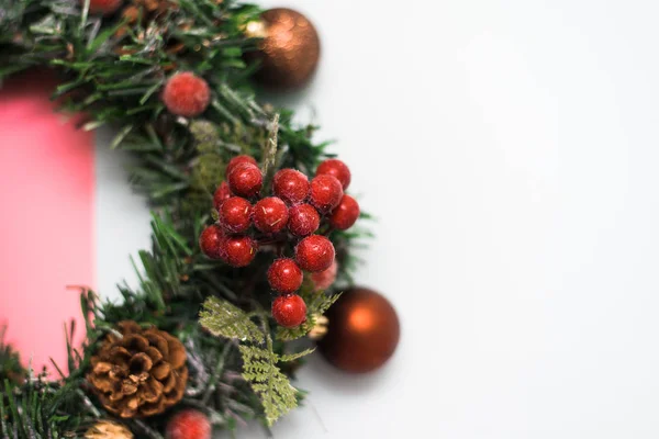 Ghirlanda di Natale composta da rami artificiali di albero di Natale, giocattoli natalizi e bacche rosse su sfondo rosa pastello e beige. vista dall'alto — Foto Stock