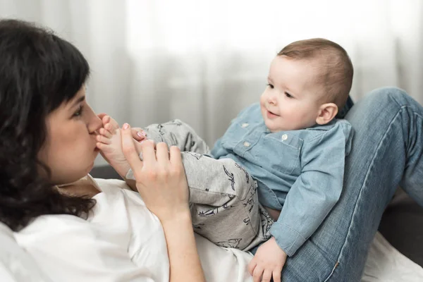Mutter küsst die Füße des Babys und spielt mit ihm in ihren Händen. glückliches Familienwochenende zu Hause. — Stockfoto