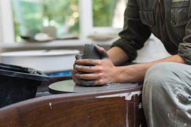 Usta, çömlekçi tekerleğindeki gri kilden ürünler yaratır. Kız seramik bir vazo oluşturur