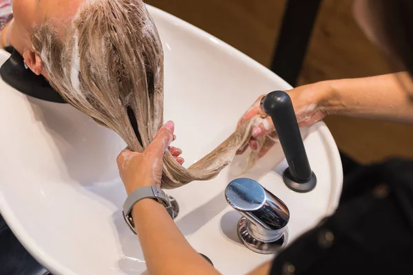 washing your hair in the cabin. a hairdresser washes hair with a shampoo to a blonde girl.