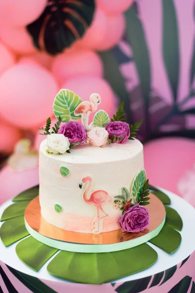 Pink cake with flamingos for the holiday. Cake with a variety of decorations, palm leaves and fresh flowers.