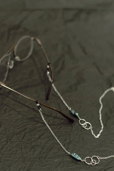 Cadeia de prata elegante com uma pérola nos óculos. tendência para corrente para óculos. Copos de bronze vintage em papel manteiga enrugada preta — Fotografia de Stock