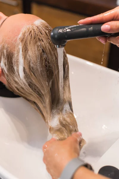 Mycie włosów w kabinie. Fryzjer myje włosy szamponem do blond dziewczyny — Zdjęcie stockowe