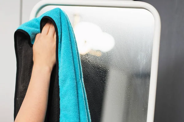 Η καθαρίστρια σκουπίζει τον καθρέφτη από τη σκόνη. Η νοικοκυρά πλένει έναν καθρέφτη στο πάτωμα με ένα μπλε πανί.. — Φωτογραφία Αρχείου