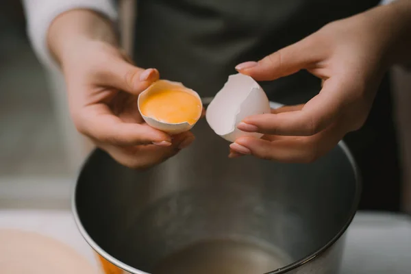 Las hembras cocinan en un delantal gris rompe un huevo en un tazón de metal. Separar la proteína de la yema — Foto de Stock