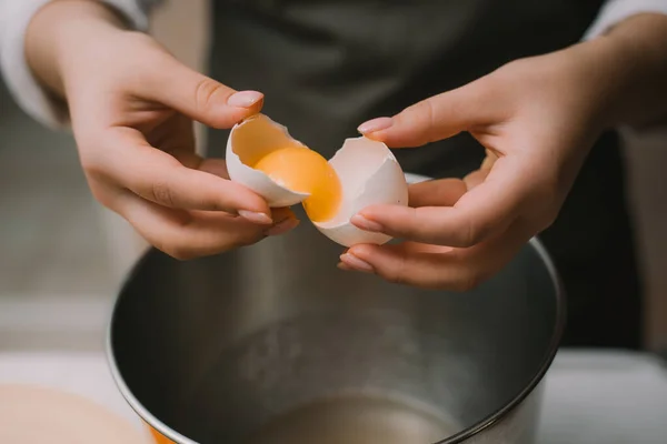 Las hembras cocinan en un delantal gris rompe un huevo en un tazón de metal. Separar la proteína de la yema — Foto de Stock