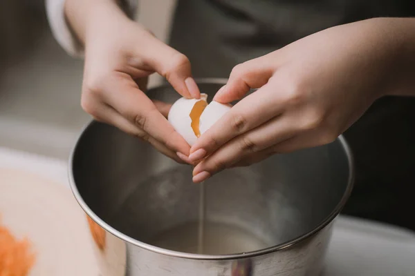 Las hembras cocinan en un delantal gris rompe un huevo en un tazón de metal. Separar la proteína de la yema Imagen De Stock