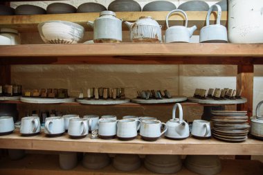 Çömlekçi atölyesinde el yapımı seramik çömlek. Atölyedeki raflarda kil tabaklar, kupalar ve çaydanlıklar var.