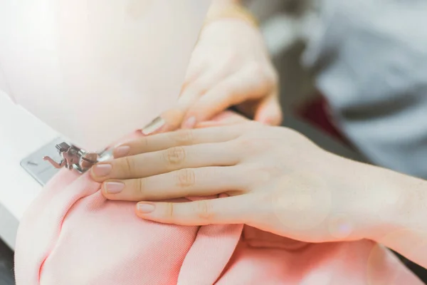 Швачка працює на швейній машинці. Дівчина шиє і тримає рожеву тканину — стокове фото