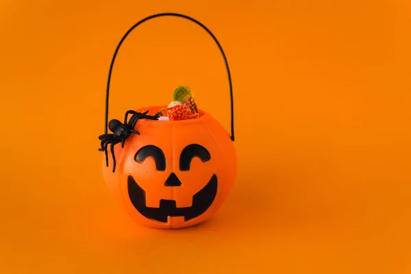 Dolcetto o scherzetto per Halloween. Secchio di zucca con dolci e ragni su fondo arancione. Dolci per bambini per Halloween. Copyspace — Foto Stock