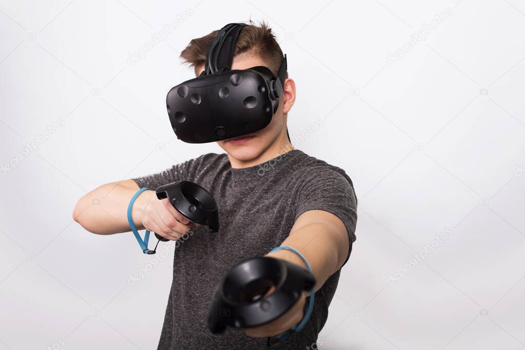 A young man holds controllers for a viar game. A teenager plays with virtual reality glasses and considers joysticks and gamepads