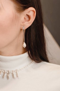 Modelde inci mücevher var. Boynunda ve kulaklarında beyaz inci küpeler ve kolye ve beyaz balıkçı yakalı genç bir kız.