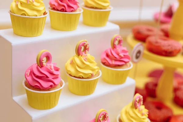 Magdalenas rosadas y amarillas con rosquillas de masilla. Dulces brillantes y alegres para las vacaciones — Foto de Stock