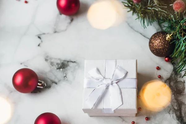 Regalo de plata sobre fondo de mármol con bolas rojas de Navidad y corona de Navidad. El concepto de Año Nuevo y Navidad, luces guirnalda amarilla y regalos para las vacaciones —  Fotos de Stock