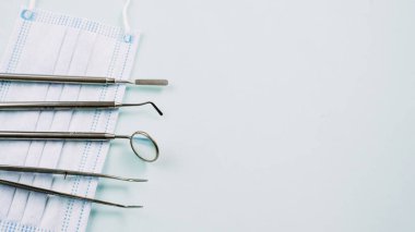 Diş aletleri koruyucu bir maskenin mavi arka planında yatar. Ayna, cımbız, mavi arka planda kazıyıcı. Reklam veya blog için şablon.