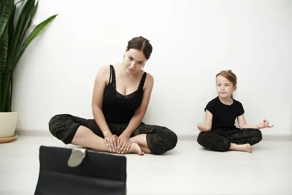 Mother and daughter are doing yoga online. Woman and little girl are watching online exercises