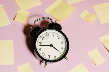 Beyaz alarm saati ve pembe arka planda sarı yapışkan notlar. Çalışma zamanı kavramı. İşyeri.