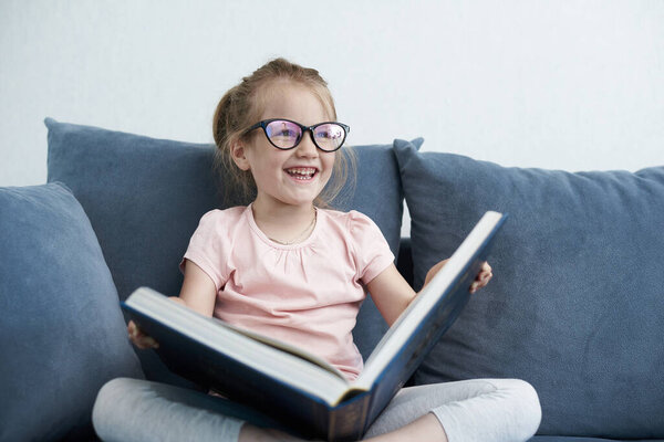 A little girl is reading book. A smiling little girl holds a book. A little girl is reading and smiling.