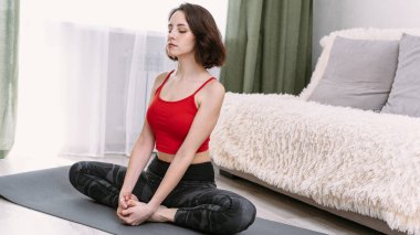 Güzel bir kadın ev içinde yoga yapıyor. Nilüfer pozisyonunda rahatlama ve meditasyon.