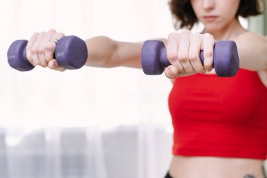 Güzel bir kadın evde dambıllarıyla spor yapıyor. Kararlı kadın evde kilo veriyor ve halterlerle egzersiz yapıyor. Spor ve eğlence konsepti.
