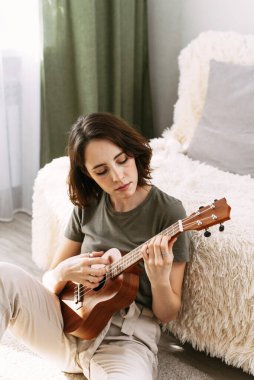 Güzel bir kadın evde küçük bir gitar çalar. Genç bir kız kendini izole ederken ukulele çalıyor..