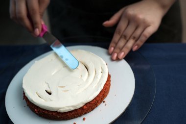 Pudra kek üzerine krema düzeyleri. Aşçı bir pasta oluşturur, topladığı ve krema ile kapsar ve bir spatula ve sıyırıcı ile düzeyleri.