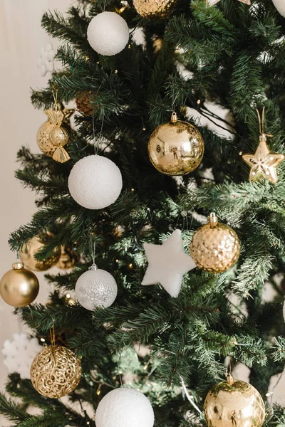在明亮的室内圣诞树上的一个金色和白色的圣诞球 背景是燃烧着的彩灯的花环 在明亮的背景上装饰圣诞树 — 图库照片