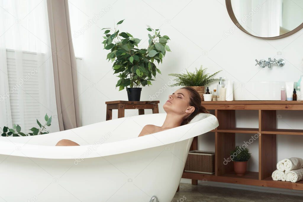 Beautiful woman relaxing in a bath tub with her eyes closed in bliss and pleasure profile view. Young woman relaxing in the beautiful bath in the retro bathroom.