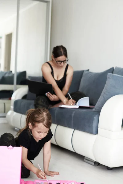 Anya és lánya otthon vannak. Anya és lánya otthon dolgoznak. Anya szörfözik a számítógépen és a lánya fest. — Stock Fotó