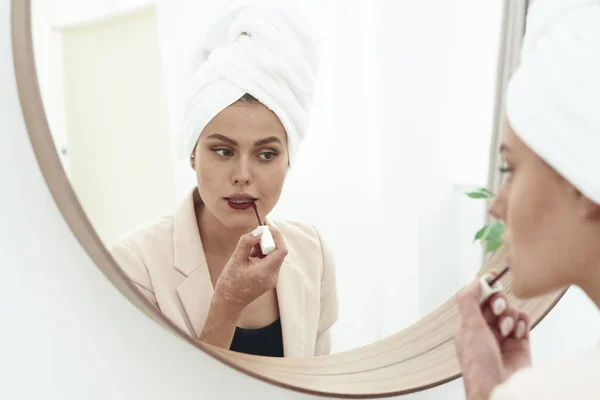 Preparándose para la cita. Retrato de una mujer hermosa, se tiñe los labios de lápiz labial de color burdeos, mirando en el espejo — Foto de Stock