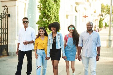 Farklı milletlerden bir grup arkadaş şehirde dolaşıp kameraya bakıyorlar..