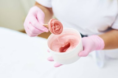 Kozmetik uzmanı pembe epilasyon macunu tutuyor..