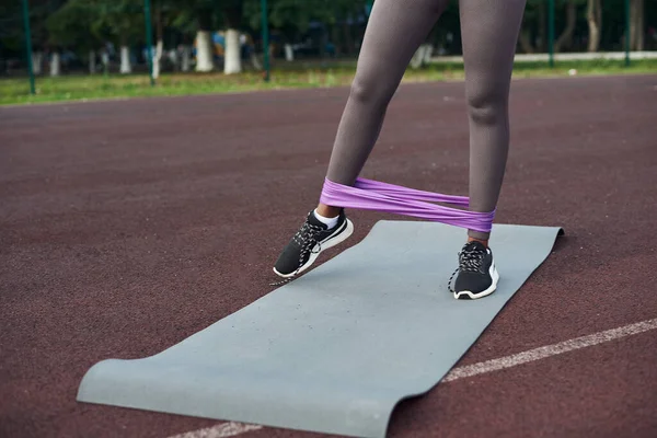 Violet elastic for fitness on female legs. Close-up. Train your legs. Training on a sports ground in the yard.
